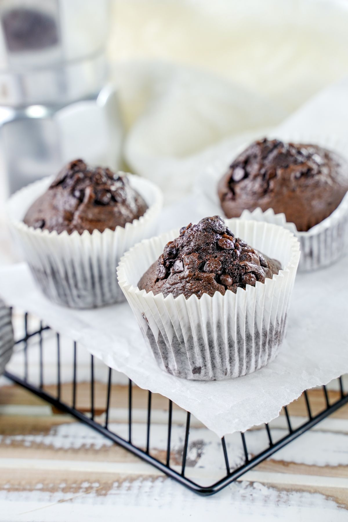 three chocolate chip muffins in white liner on upside down wire basket