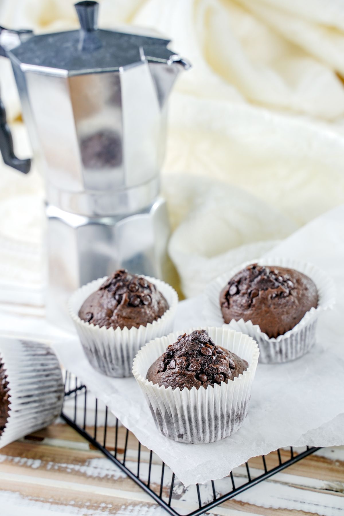 white liners on chocolate muffins sitting on table beside silver coffee pot