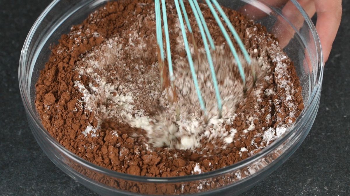teal whisk in glass bowl of cocoa and flour