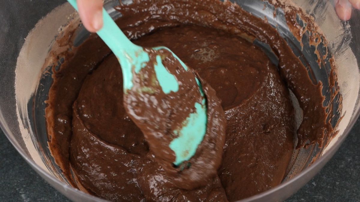 teal spatula stirring wet and dry ingredients in glass bowl into chocolate batter