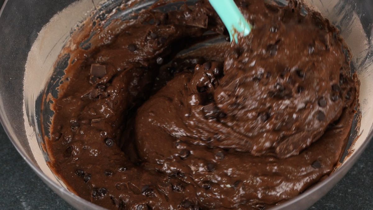 teal spatula stirring chocolate chips and chunks into chocolate batter