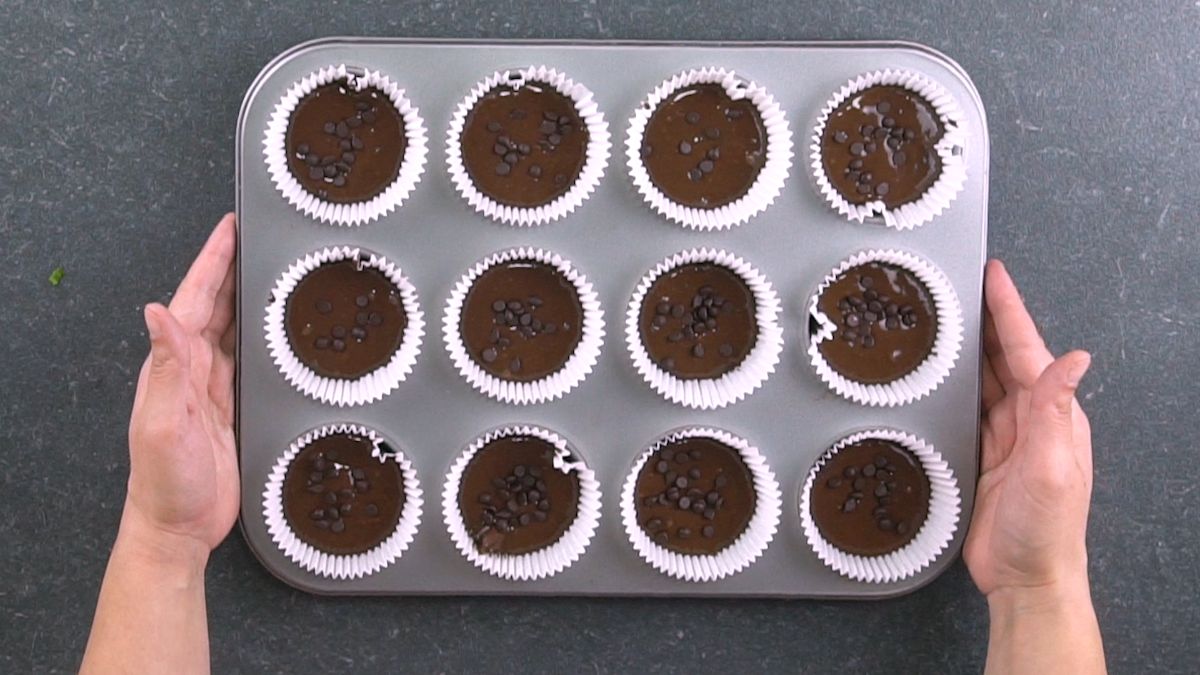 muffin tin with white liners filled with chocolate batter