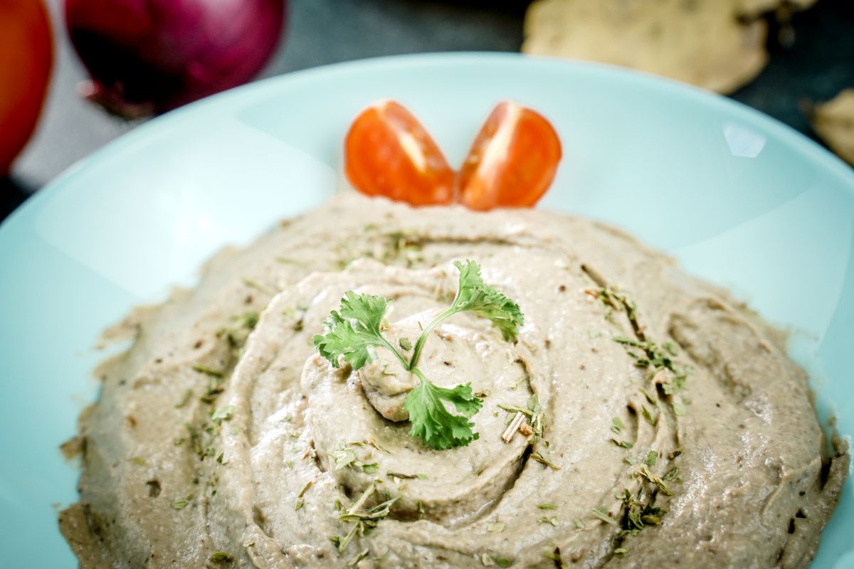 teal bowl of baba ganoush with sliced tomatoes