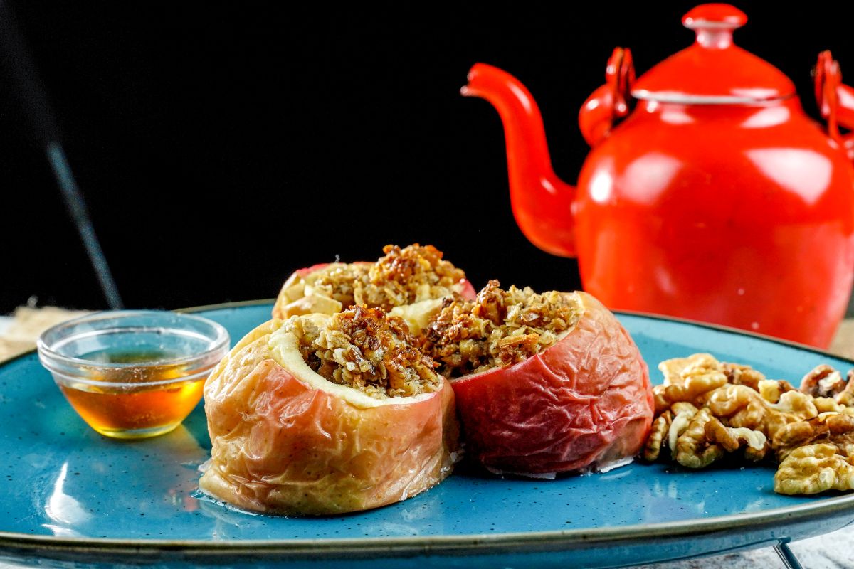 baked apples on blue plate with black background and red tea pot in background