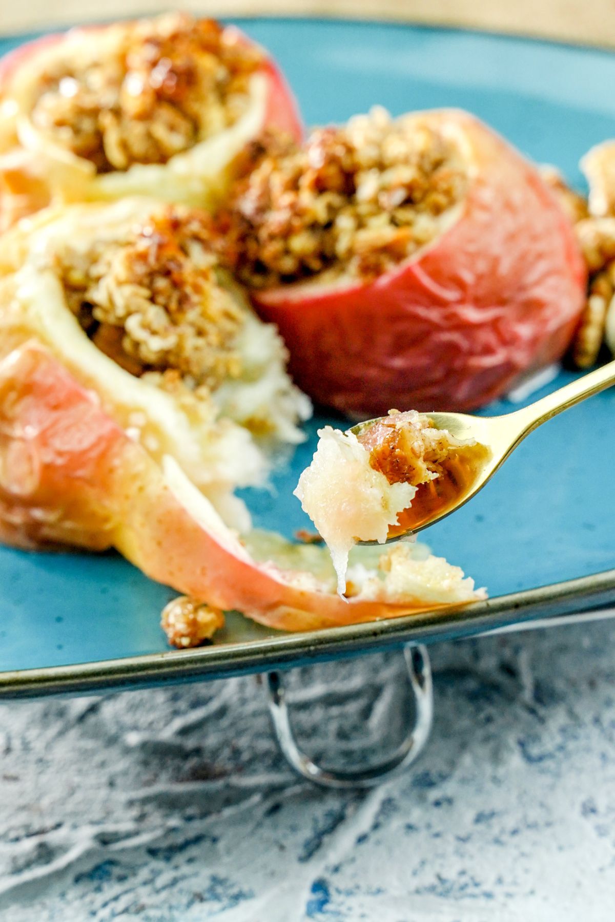 spoon of apple with oats over blue plate of stuffed apples