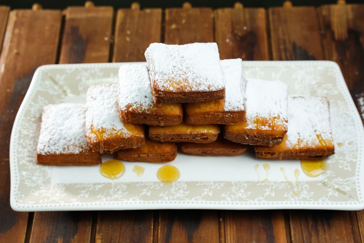 white rectangle platter stacked with tower of beignets coated in powdered sugar and honey