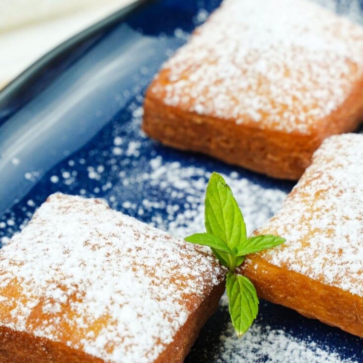 four beignets on blue platter with powdered sugar on top