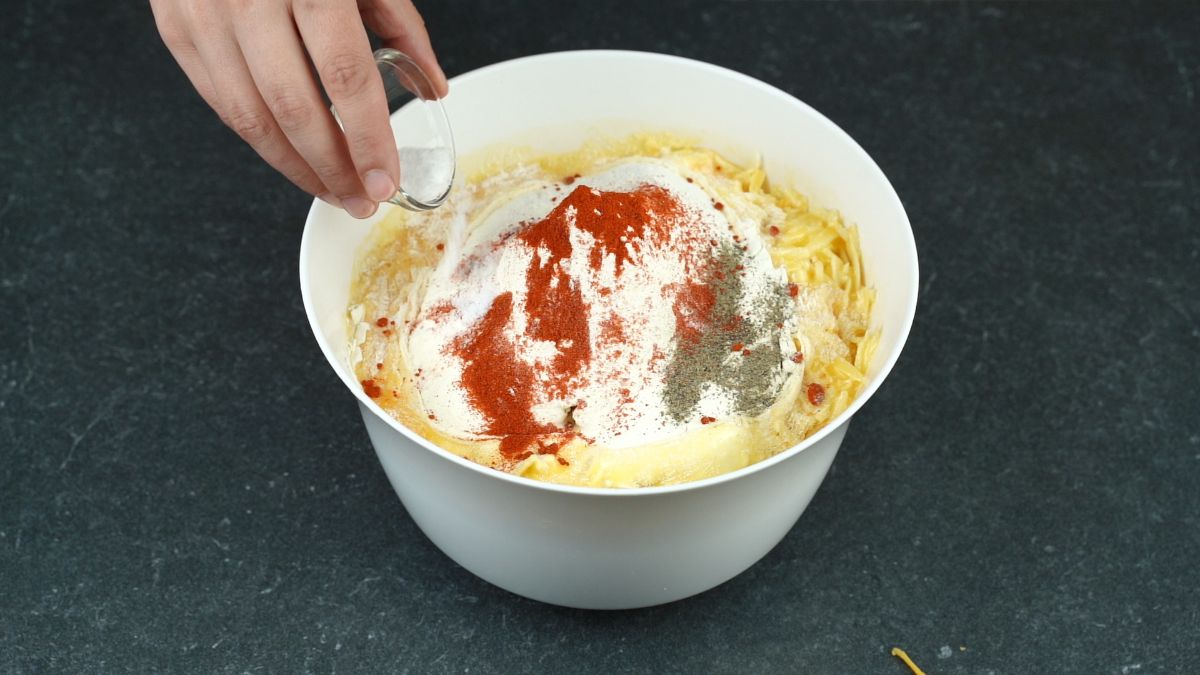 hand sprinkling salt into white bowl of cheeses and flour