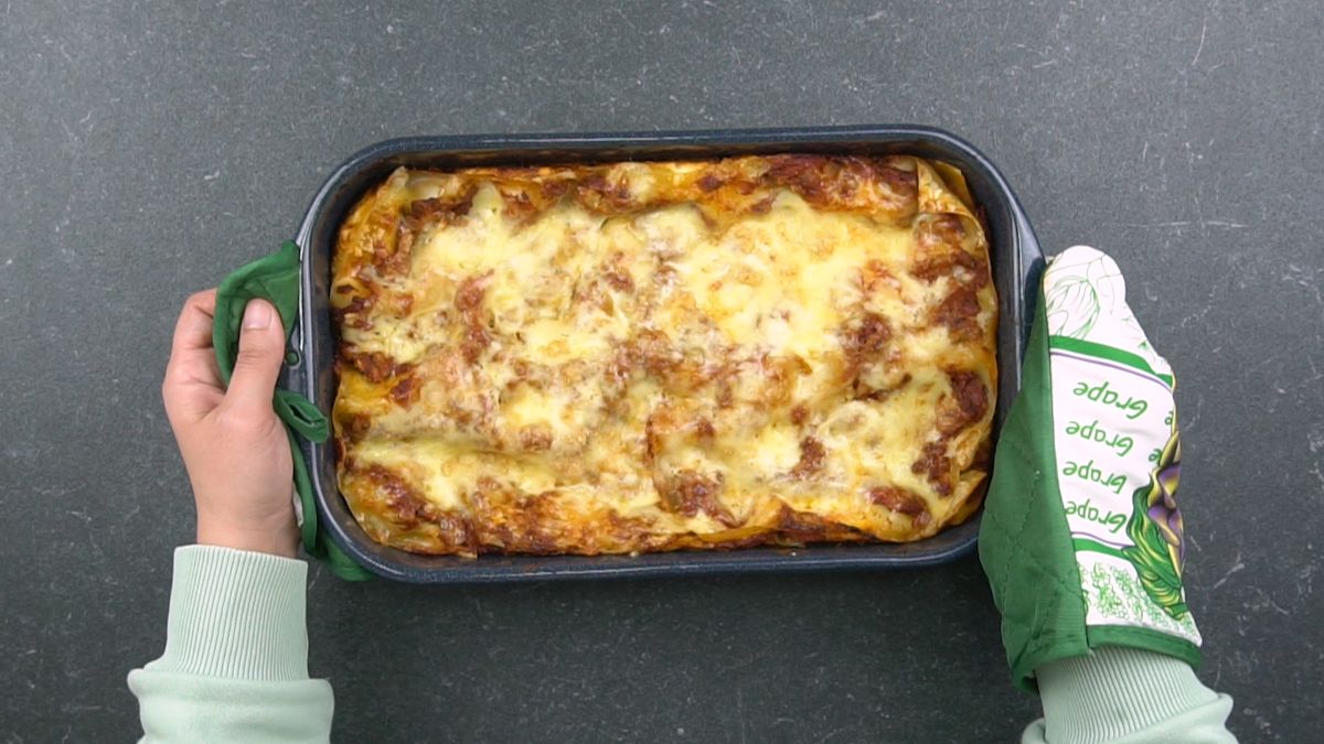 hands holding baked lasagna on table with oven mitts