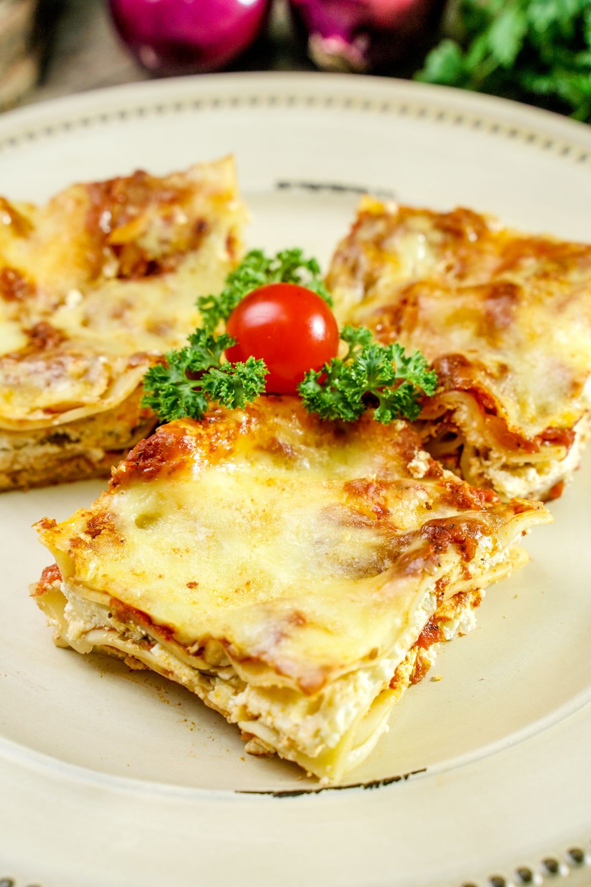 three slices cheese lasagna on cream plate with herbs and tomato in center