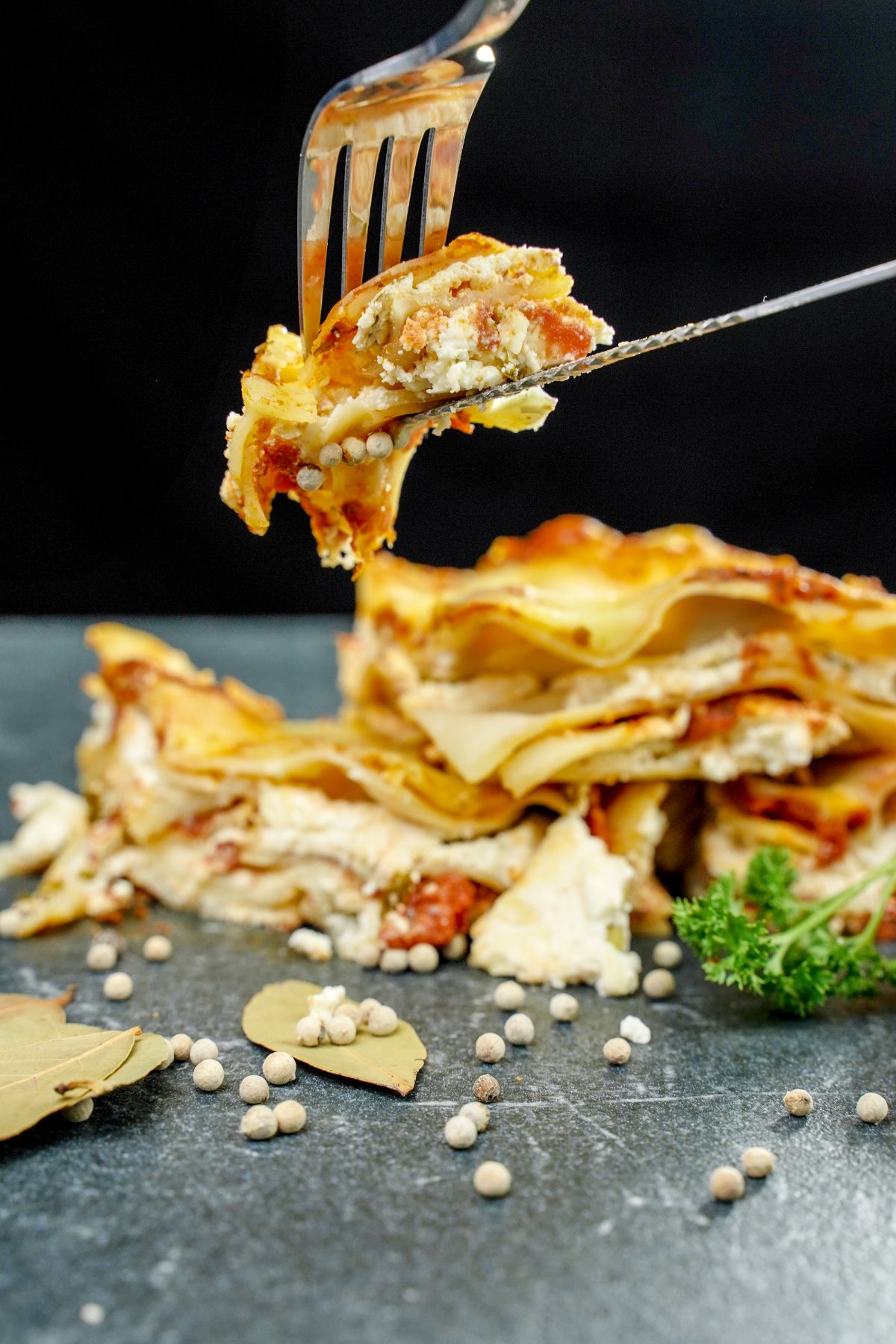 fork and knife holding bite of lasagna above stacks of lasagna pieces