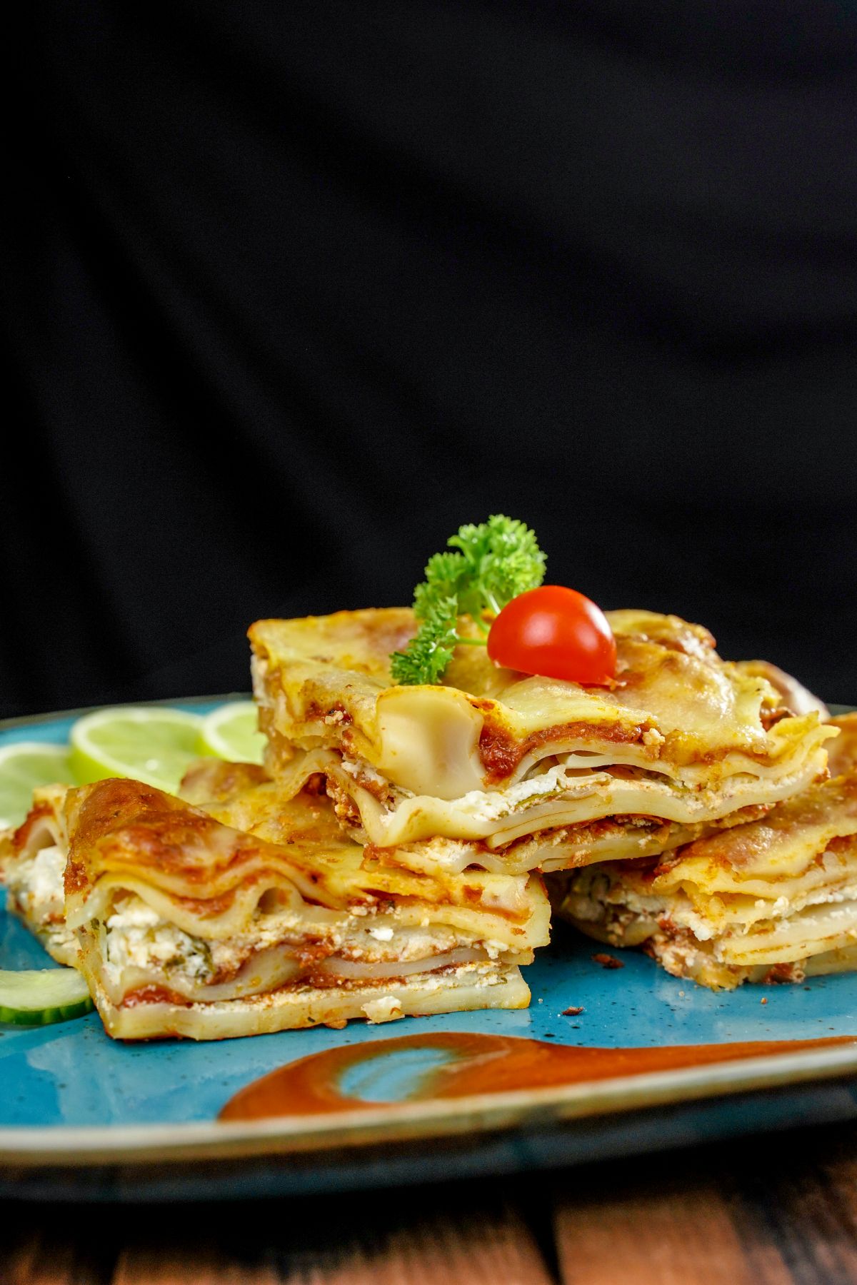 slices of lasagna stacked on teal plate with black background