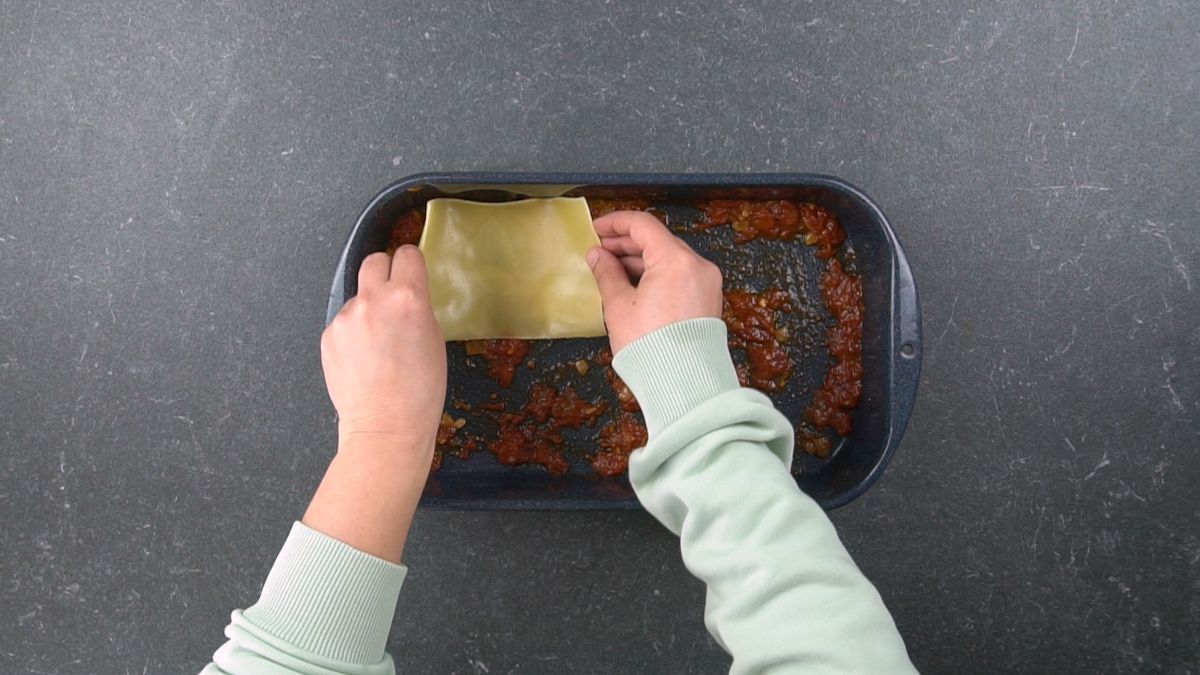 hands putting lasagna noodle into baking dish
