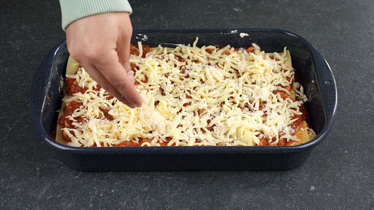 hand sprinkling cheese on top of lasagna