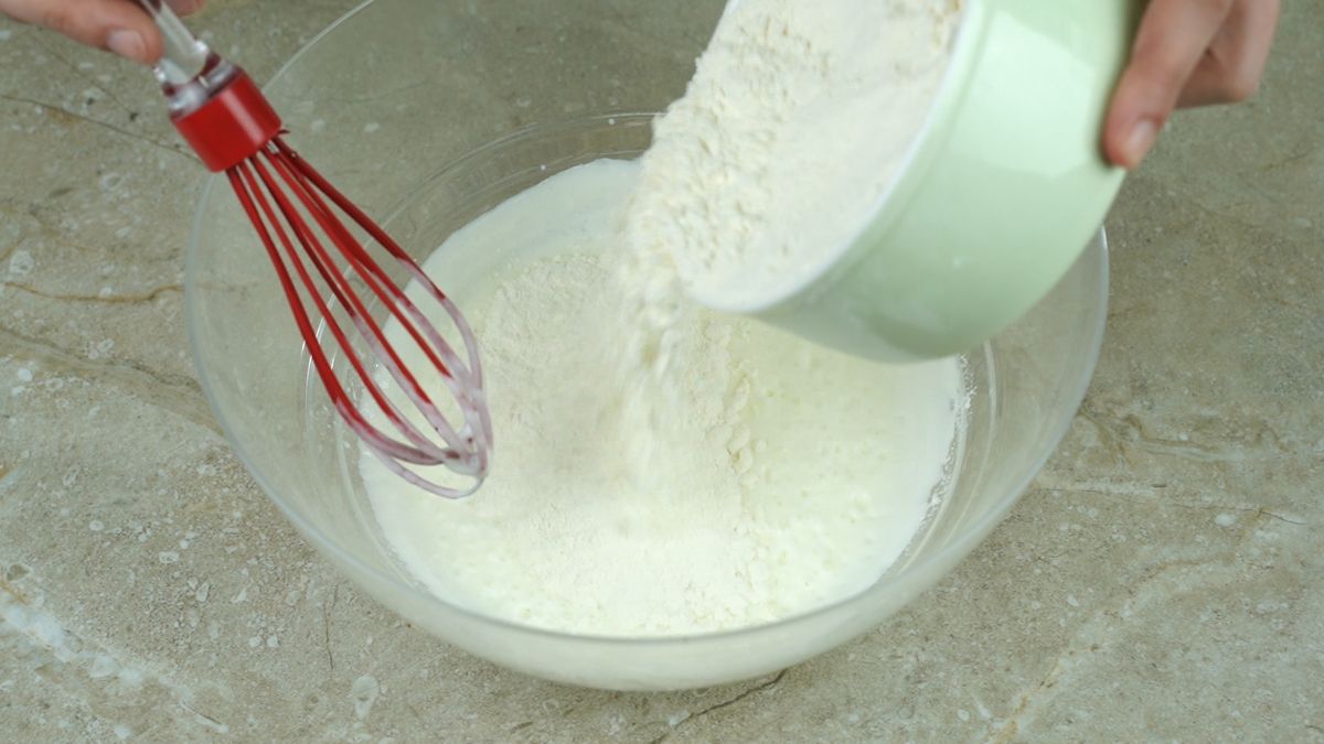 red whisk in bowl with flour being poured into it