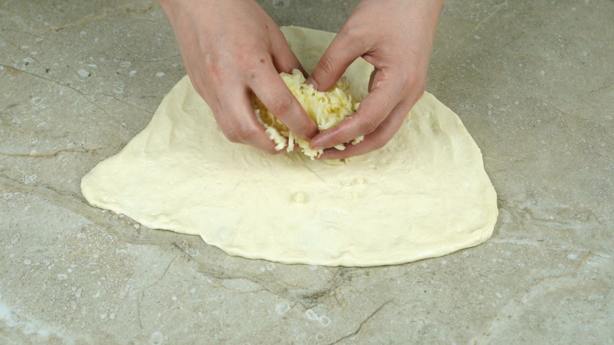 hands putting cheese on round of dough