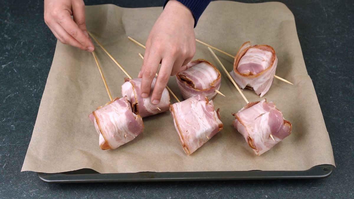 hand putting skewer into bacon covered meatball
