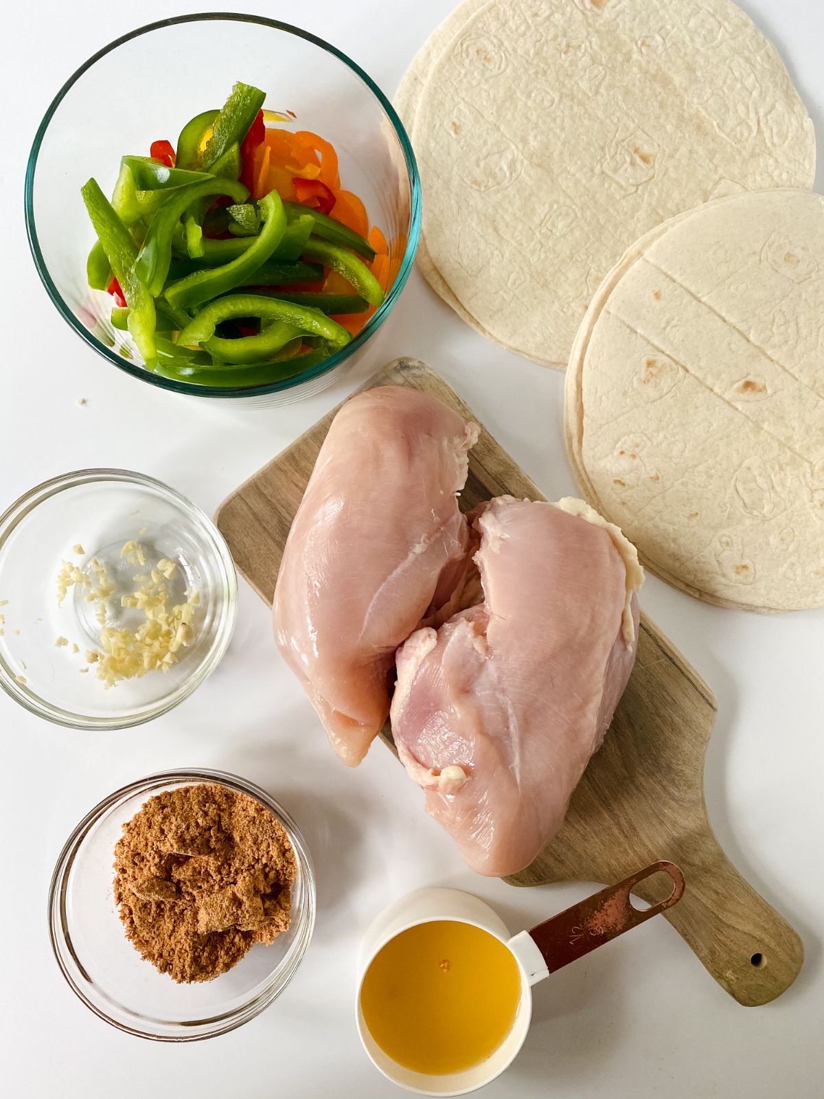 raw chicken on cutting board by bowl of peppers and flour tortillas