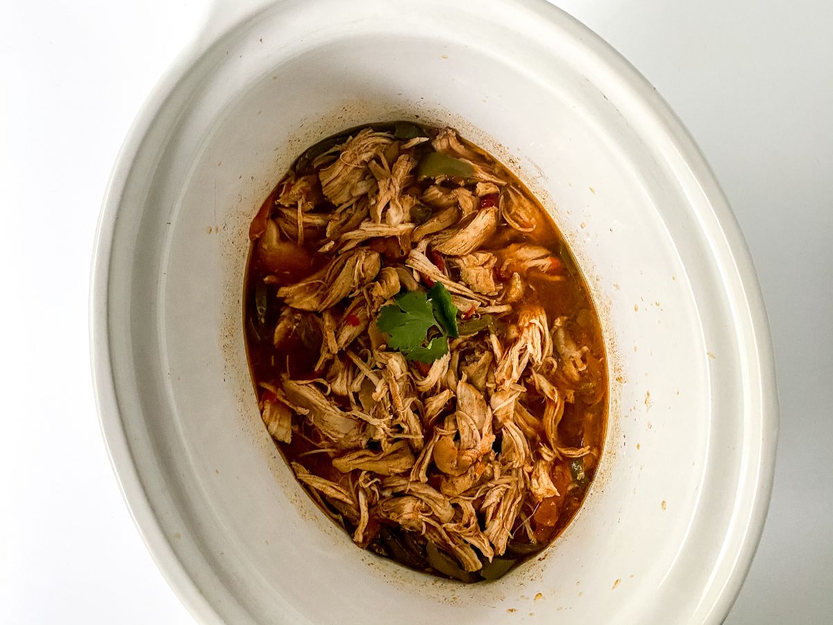 white slow cooker filled with shredded chicken in sauce