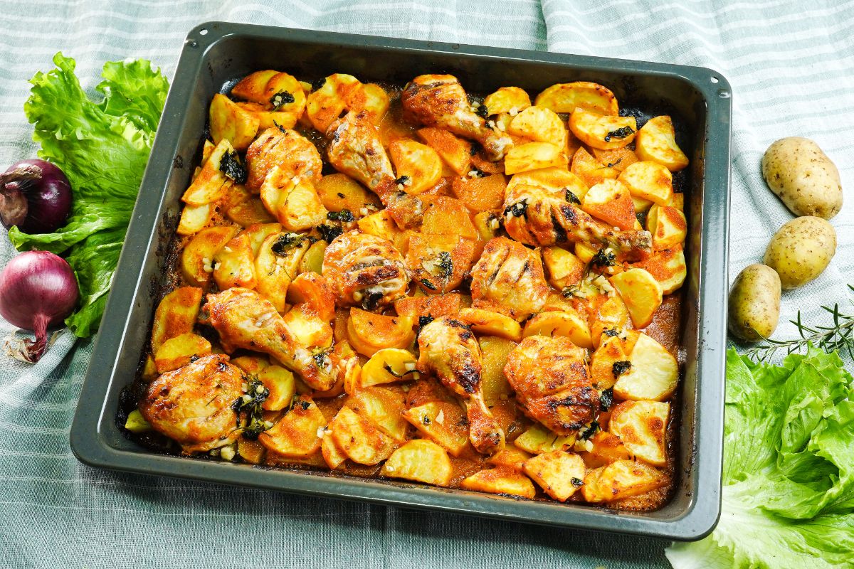 square metal baking sheet of potatoes and chicken roasted in red sauce