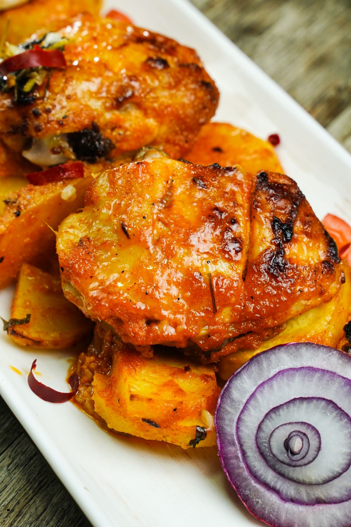 chicken thighs on top of potatoes by red onion on white platter