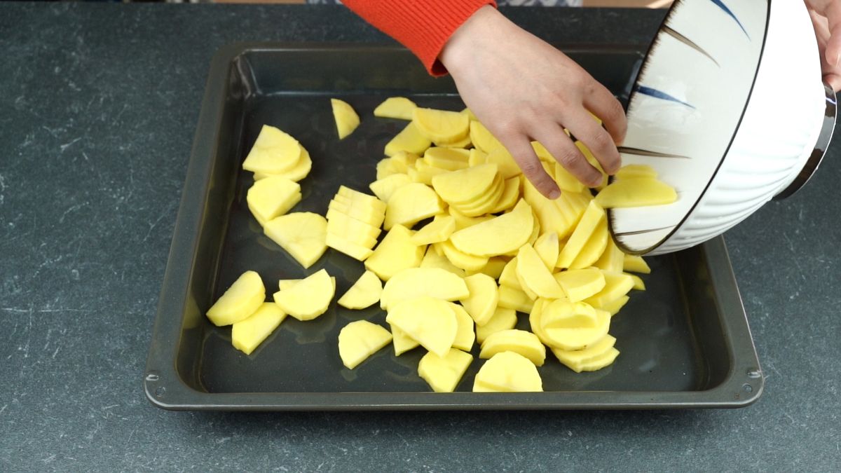 hand spreading potatoes over baking sheet
