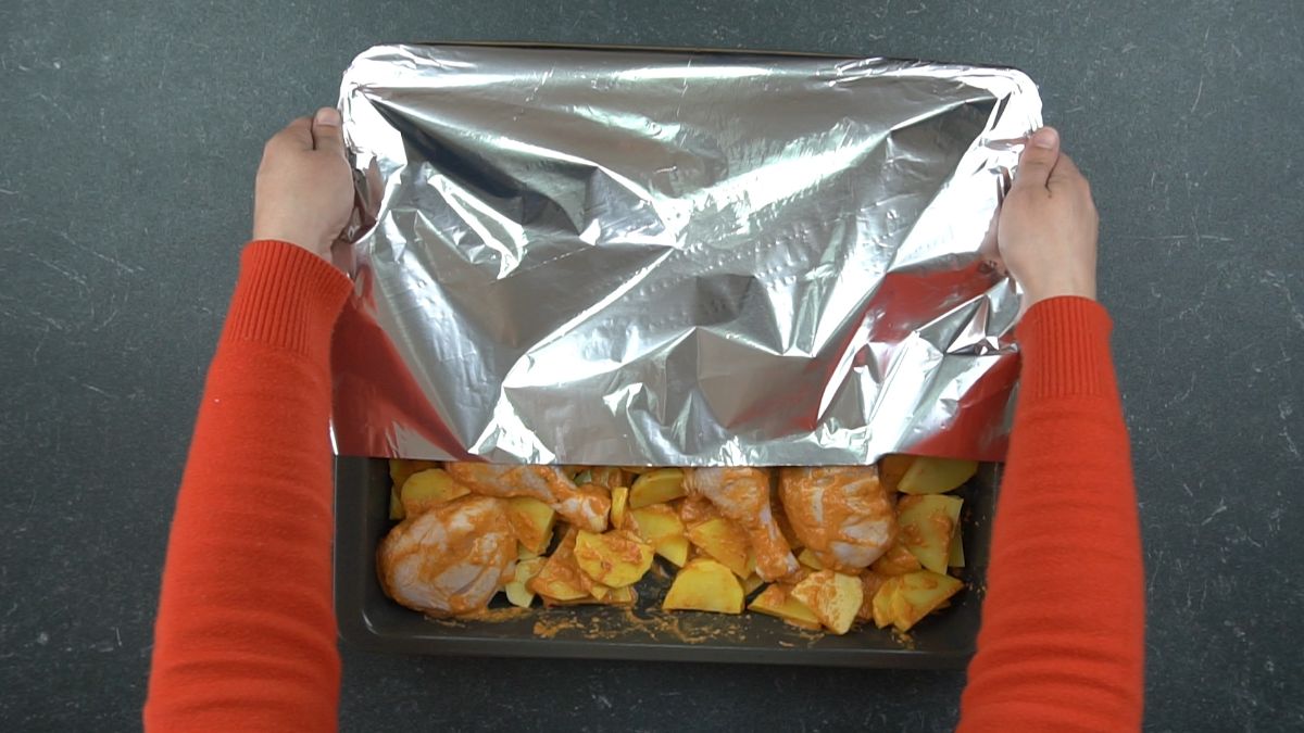 foil being put on top of chicken and potatoes on sheet pan