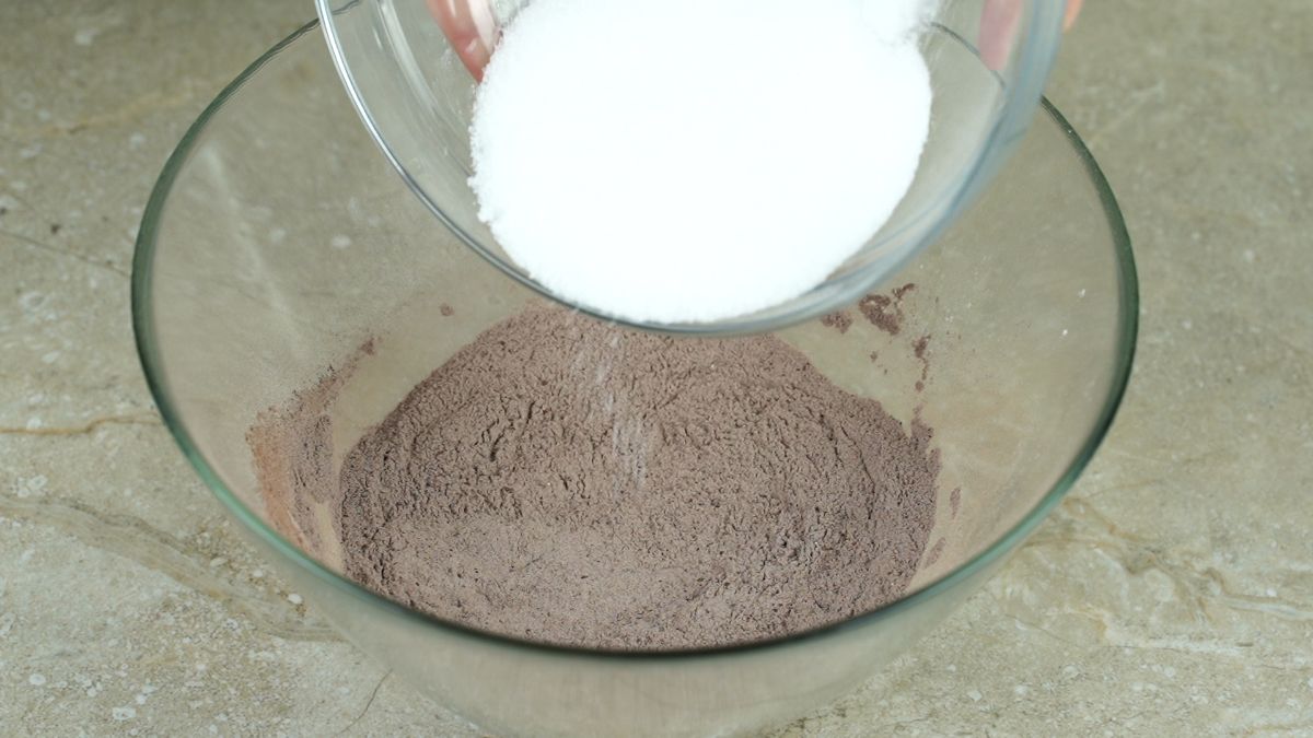 glass bowl with sugar being poured over brown ingredients