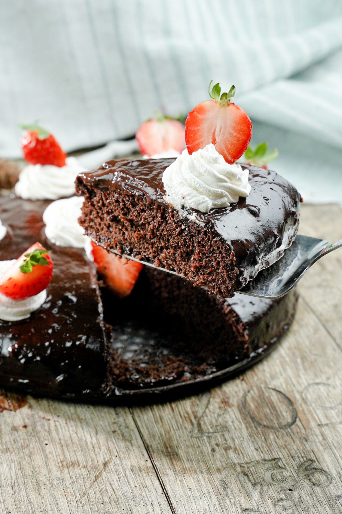 spatula holding slice of chocolate cake above rest of cake topped with cream and strawberries