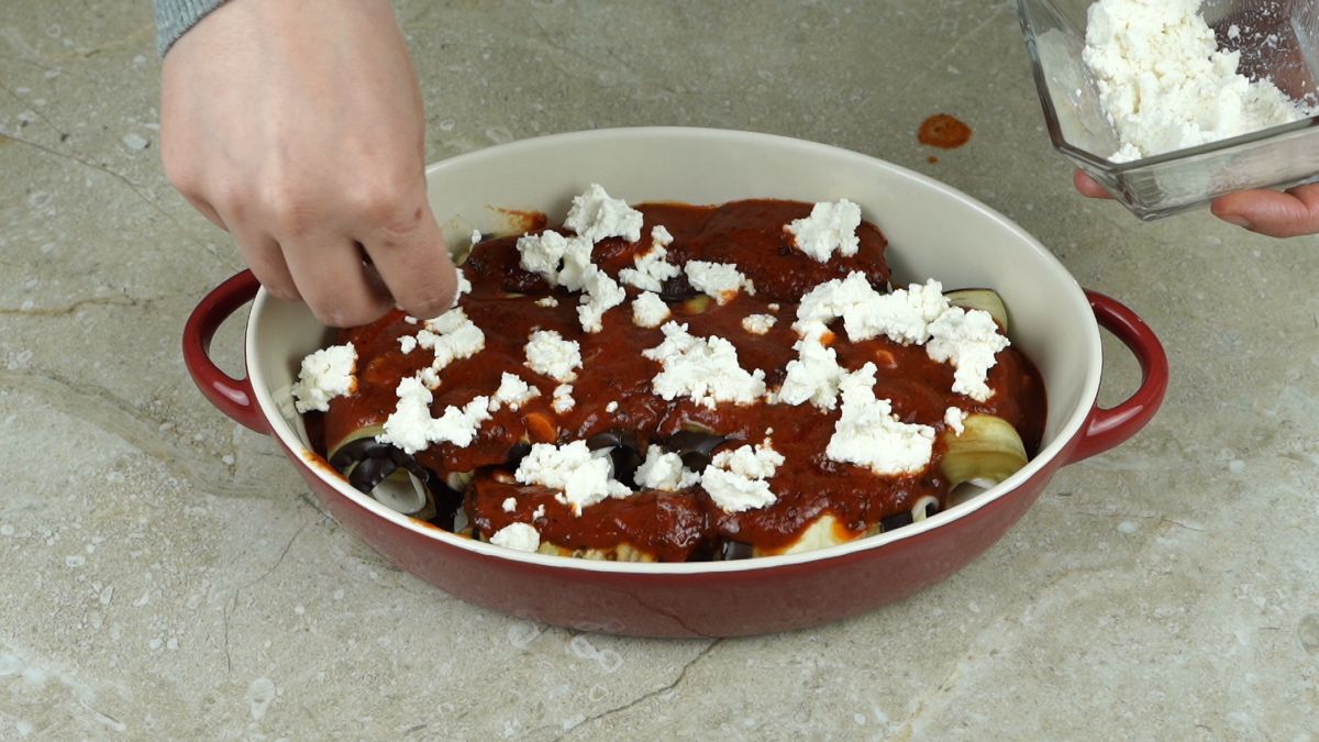 hand adding cottage cheese on top of eggplant rolls in baking dish