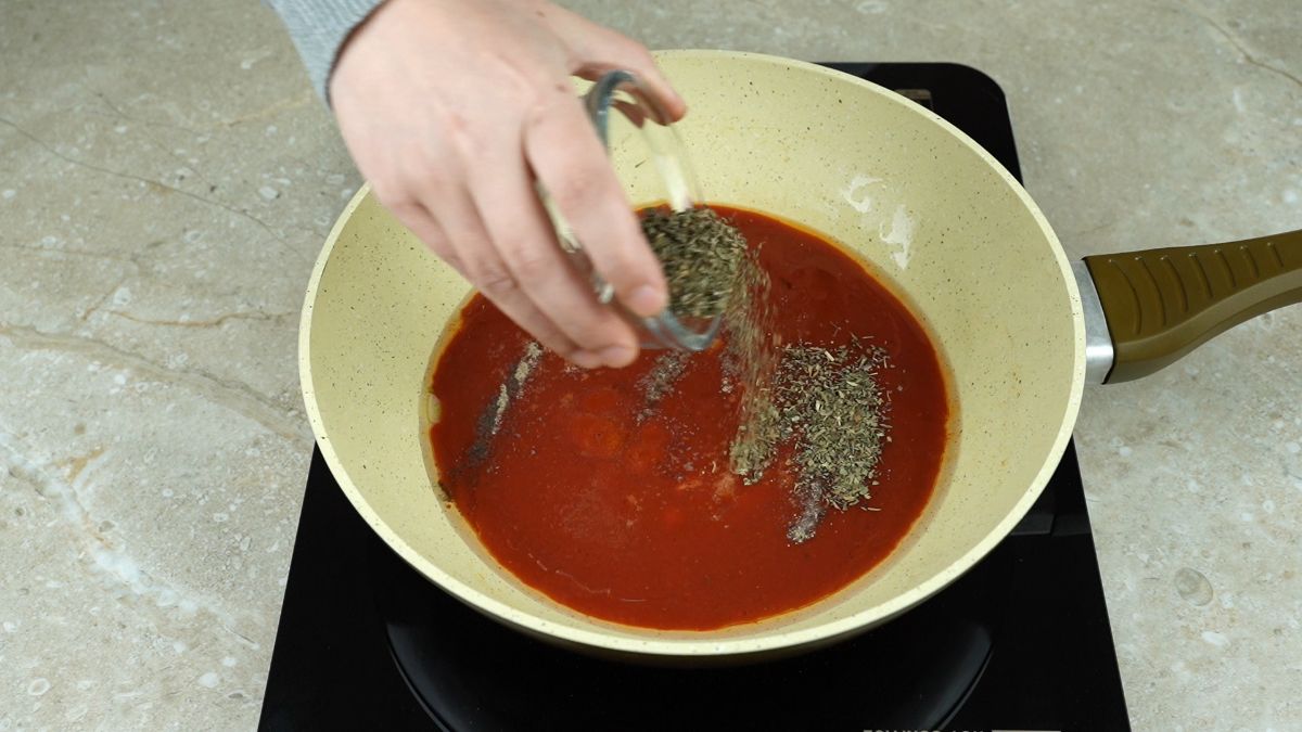 hand pouring herbs into skillet of sauce