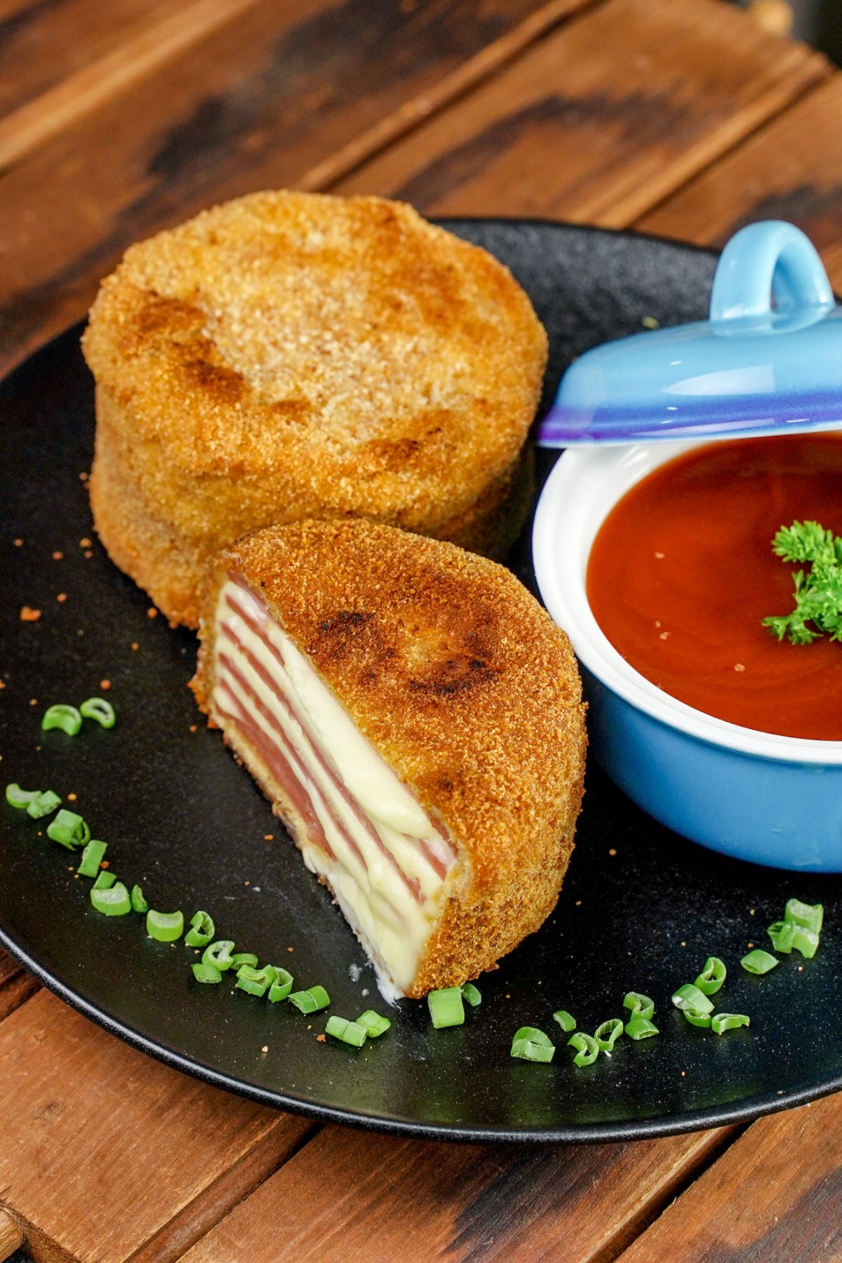 fried ham and cheese on black plate with blue bowl of soup in background 