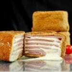 stacked ham and cheese cutlets on table with one cut in half at front