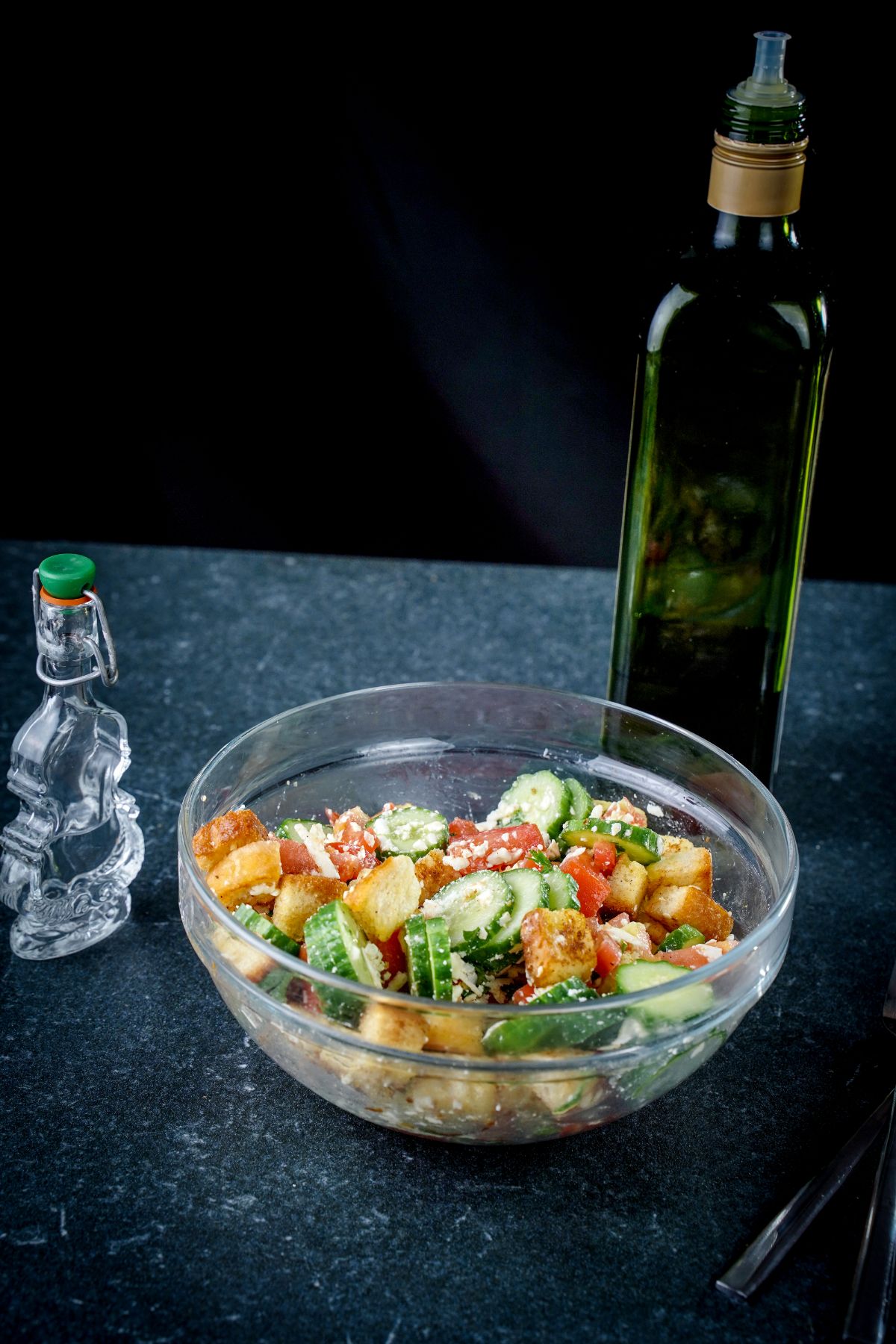 glass bowl of panzanella next to salt shaker on grey table