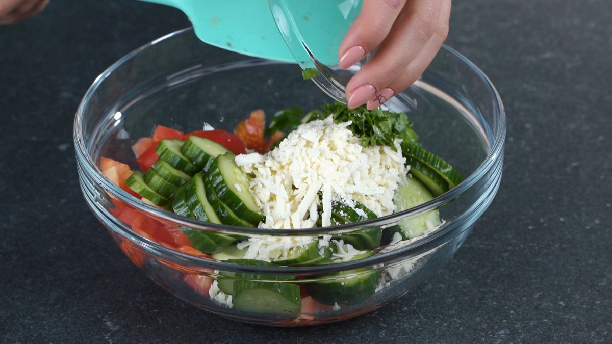 hand pouring cheese into bowl of salad