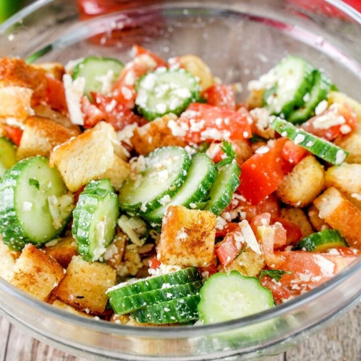 large glass bowl of cucumber and croutons on light wood table