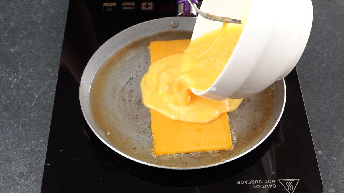 white bowl of eggs being poured over top of sliced cheese in skillet