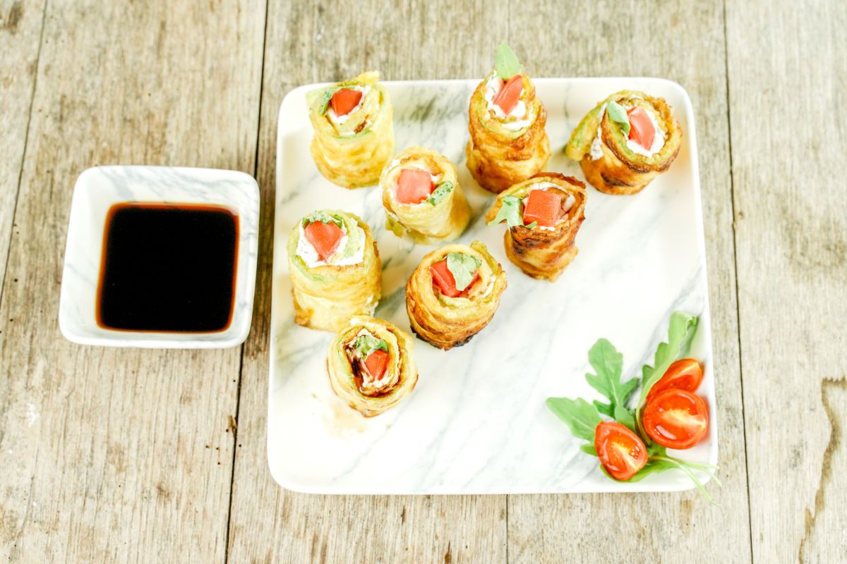 square white plate of zucchini roll ups on wood table by ramekin of soy sauce