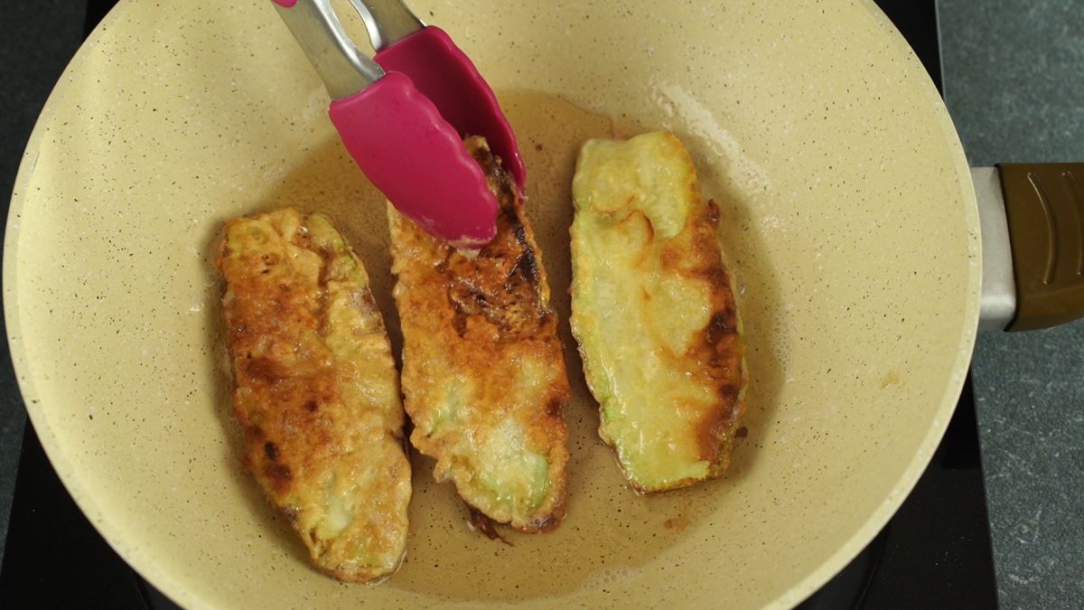 pink tongs moving zucchini out of oil in skillet