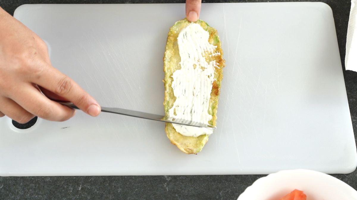 knife spreading cream cheese onto zucchini slice