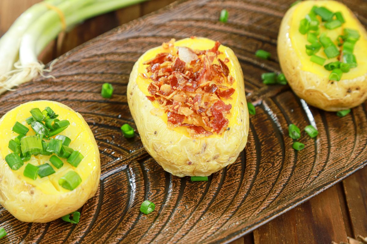 three potatoes on wood platter with bacon and chives