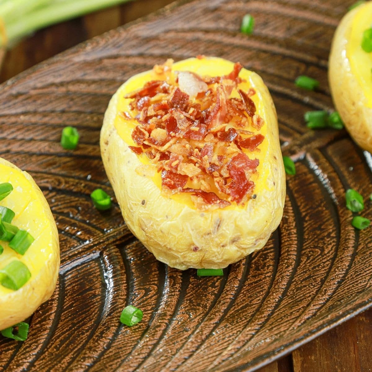 three potatoes on wood platter with bacon and chives