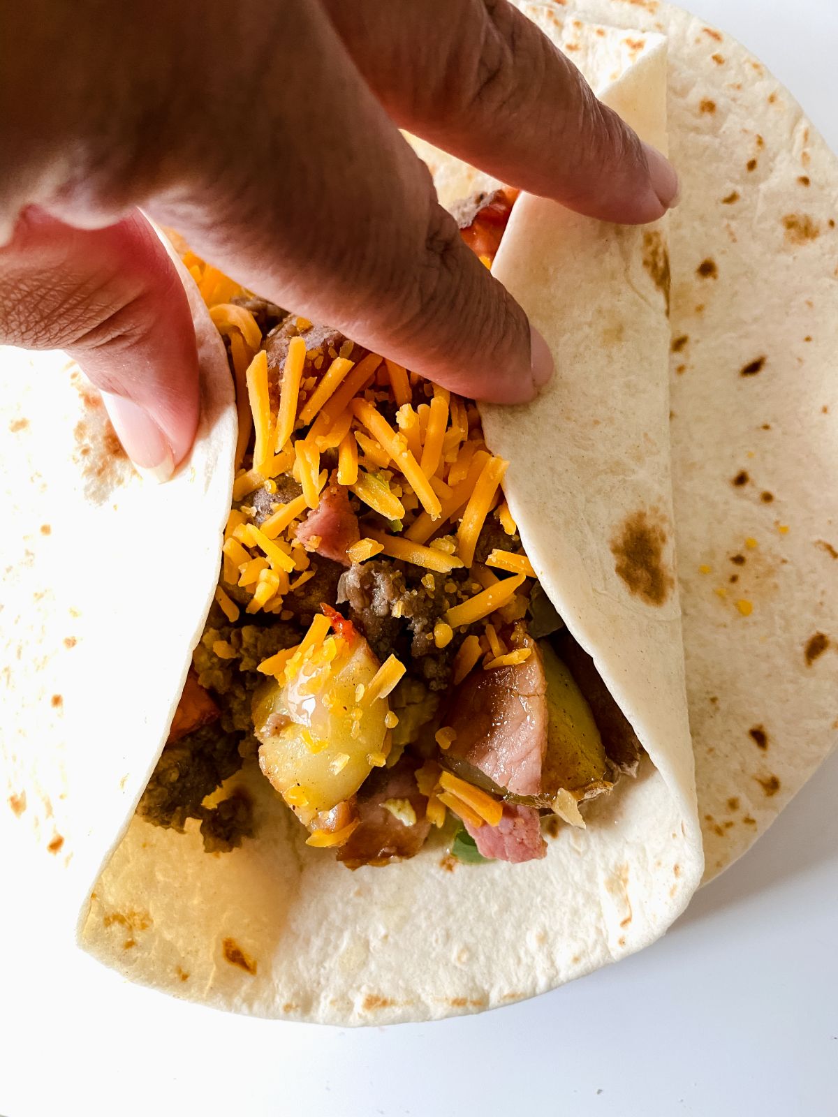 hand folding tortilla over ingredients in breakfast burrito