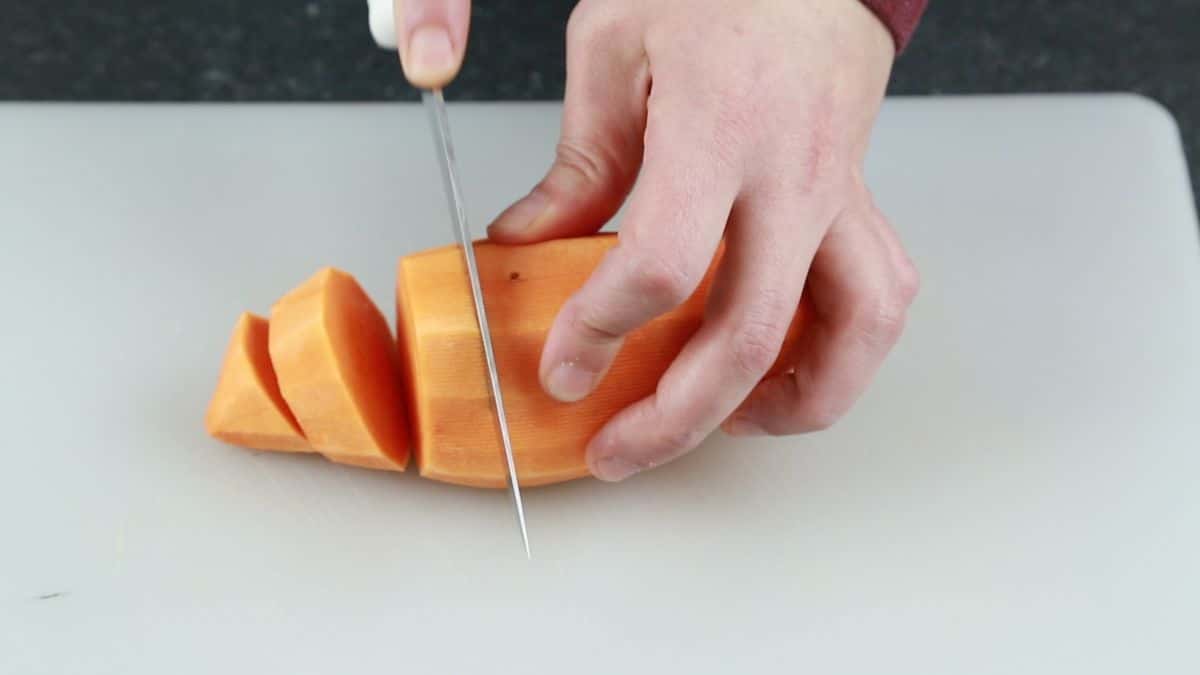 hand slicing sweet potato on white cutting board