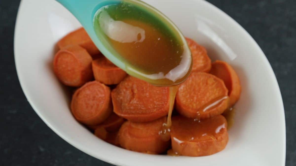spoon pouring sugar syrup over cooked sweet potatoes