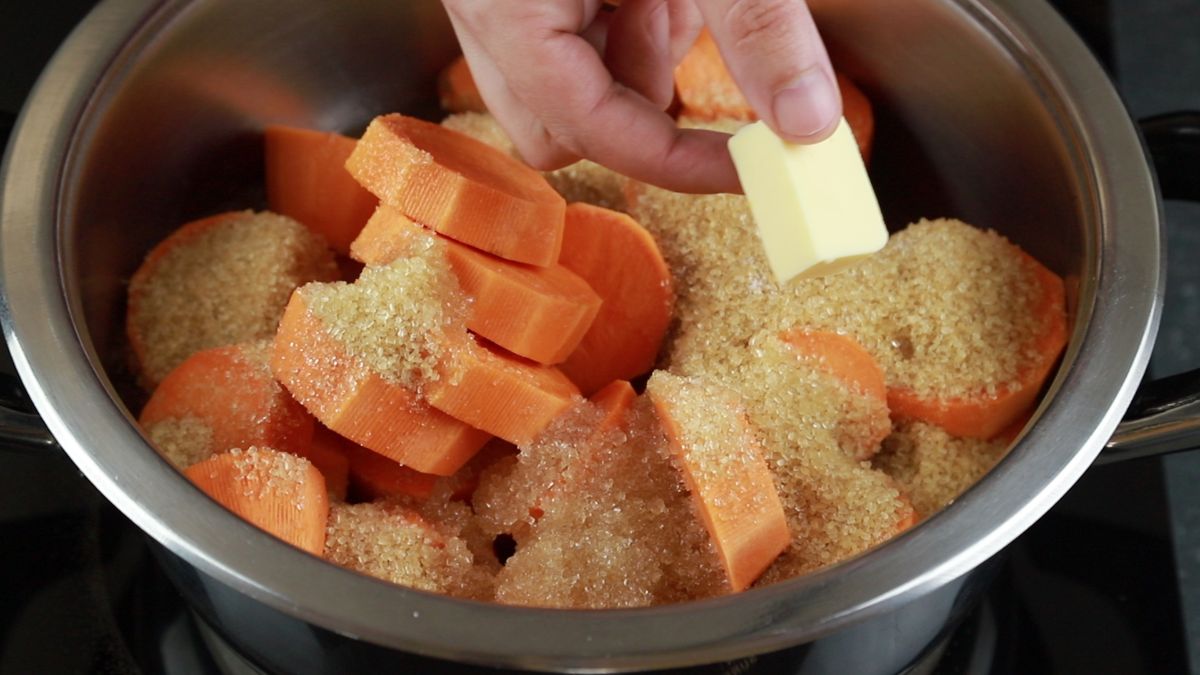 hand adding butter to saucepan of sweet potatoes