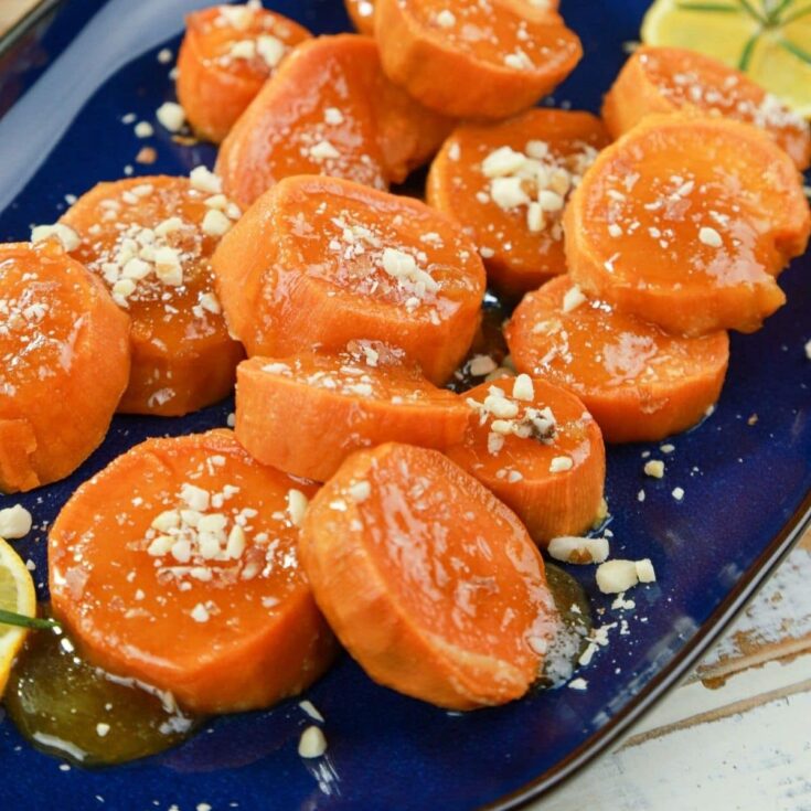 candied sweet potatoes on blue platter with orange beside platter