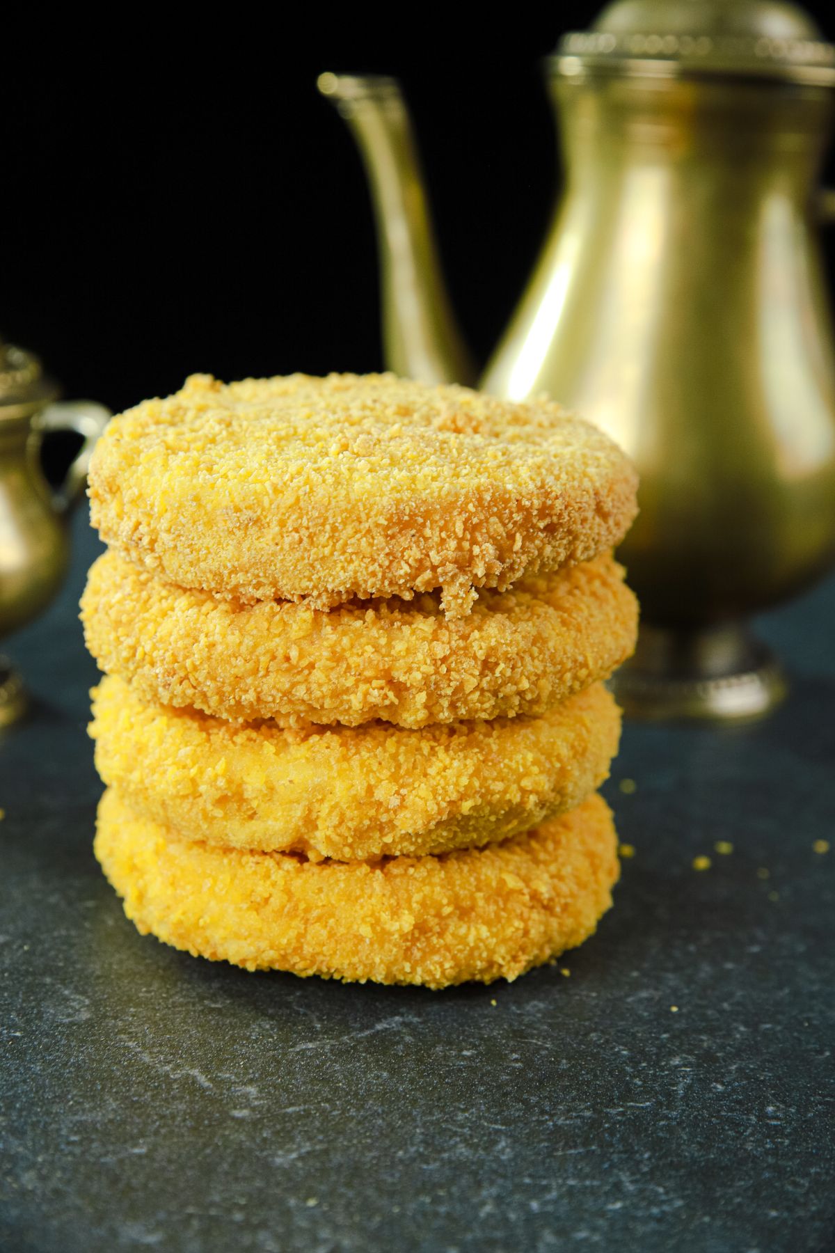 gold kettle behind stack of fried bread on black table