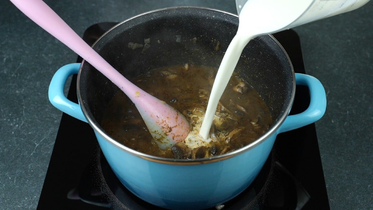 milk slurry being poured into blue saucepan of soup