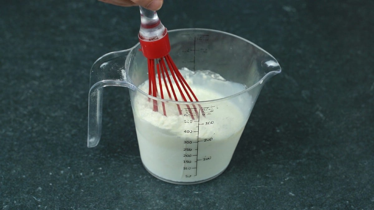 red whisk in measuring cup with flour and milk